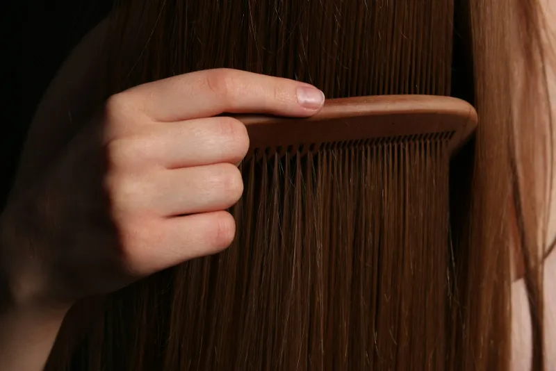 REHAB.: single-dose hair oil capsules, moisturisers and bundles A hand running a wooden comb through long, straight brown hair