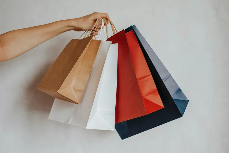 Hand holding several colourful paper shopping bags