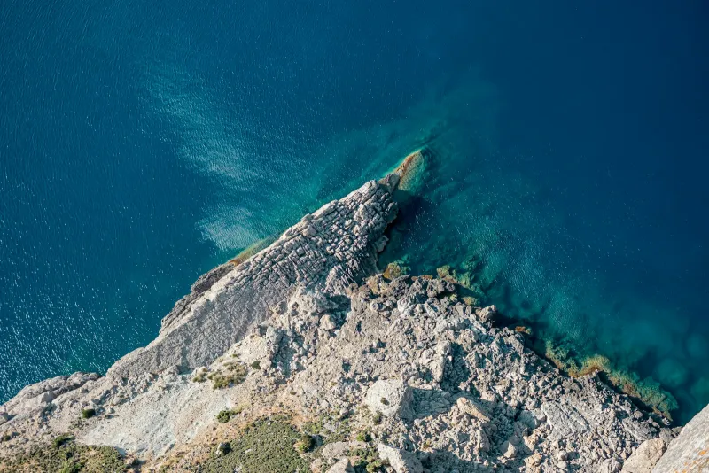 Aerial view of a rocky headland dropping into clear turquoise water on Mallorca's west coast