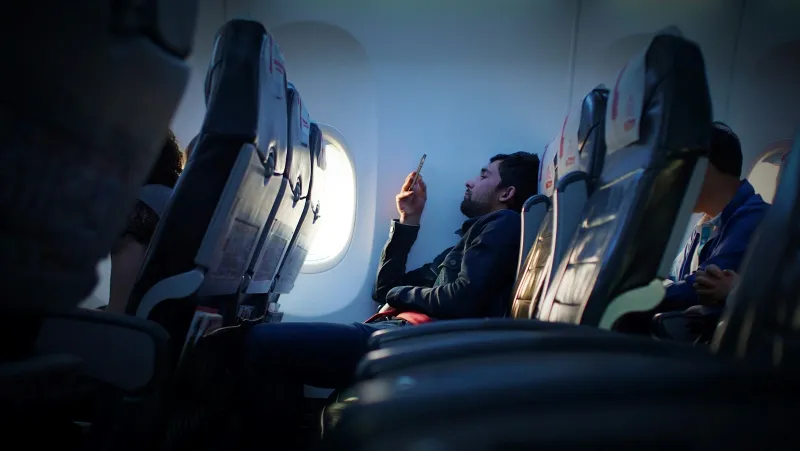 Passenger in a window seat on a plane looking at a smartphone