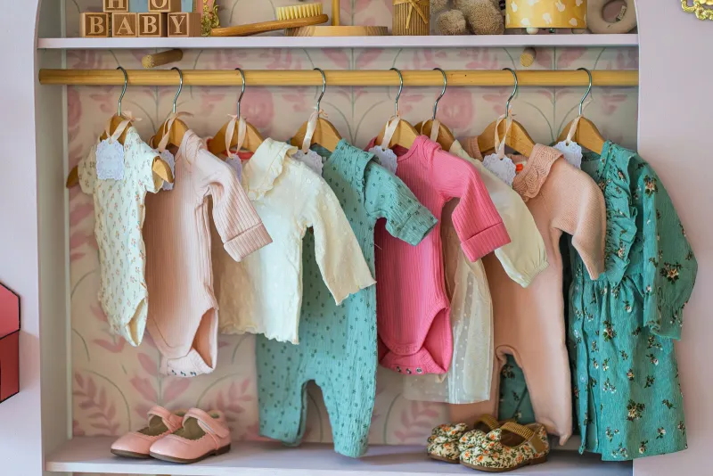 Pastel baby bodysuits and outfits on wooden hangers above small shoes