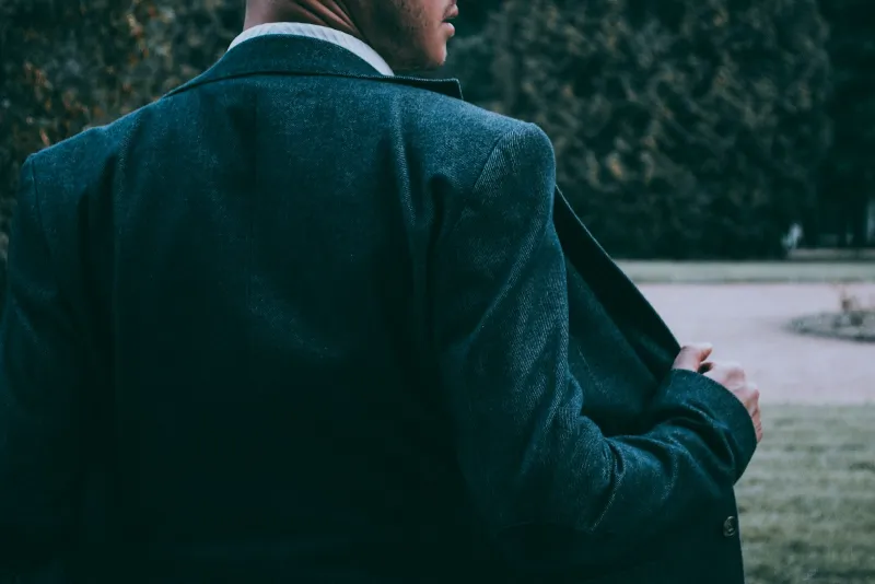 Man in a dark tweed blazer seen from behind in a garden