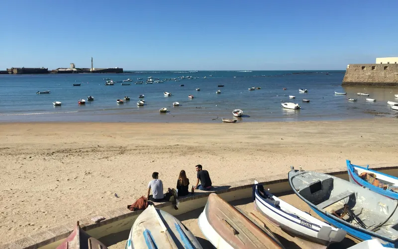 Fishing boats moored in the bay at La Caleta beach in Cádiz under a clear blue sky