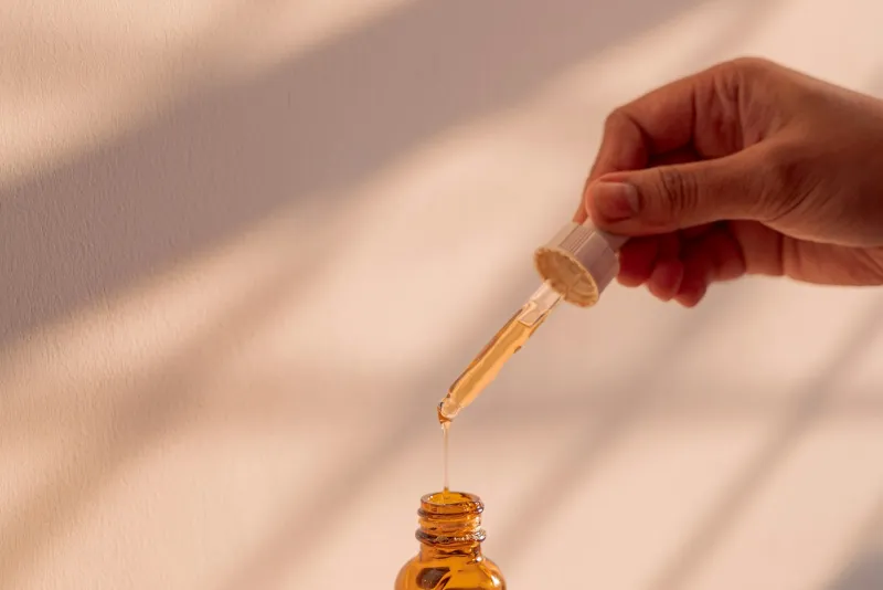 A dropper releasing a drop of golden serum into an amber glass bottle
