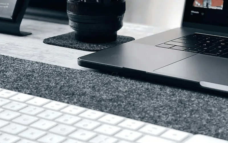 A camera lens on a felt coaster beside a laptop and keyboard on a desk