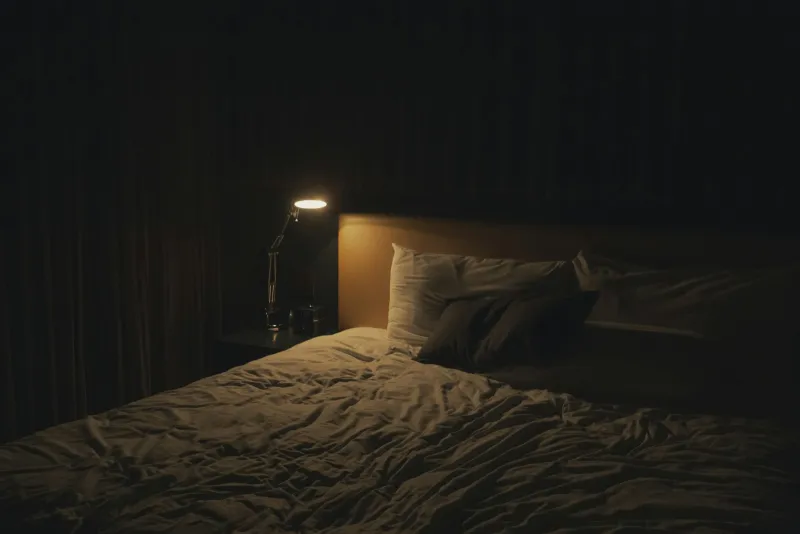 Bedside table lamp glowing next to a made bed
