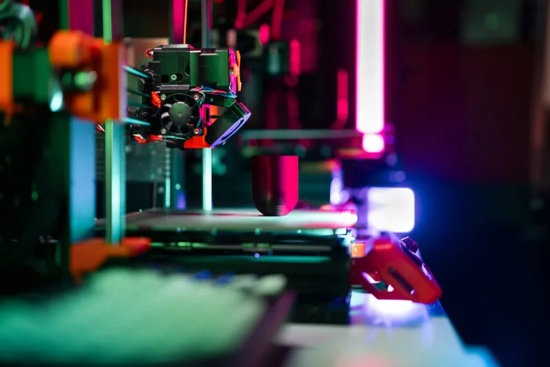 Close-up of a 3D printer's print head building a small object under pink and blue light