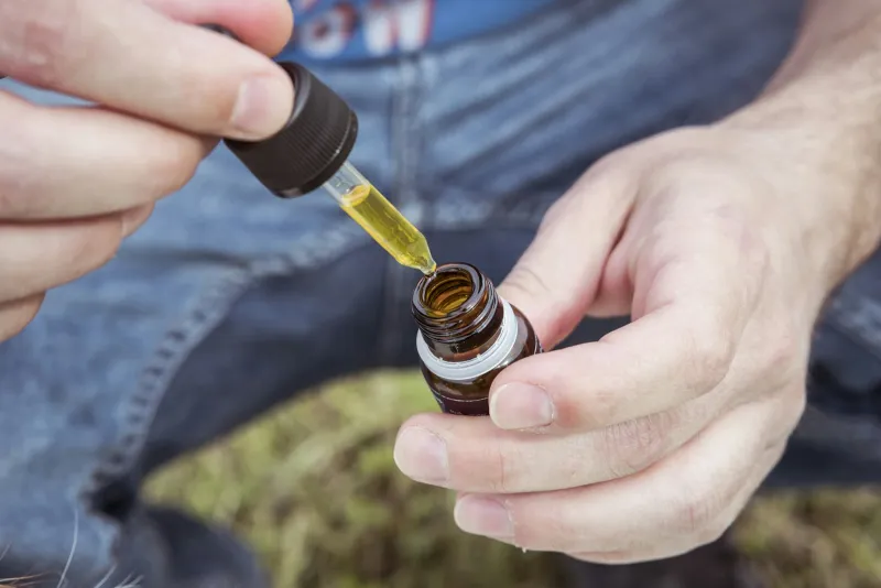 Hands holding a small amber dropper bottle of oil outdoors