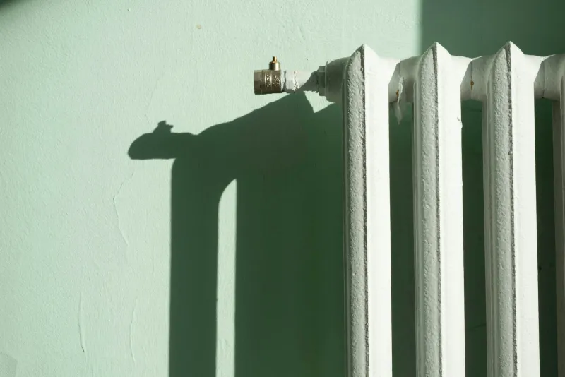 White cast iron radiator and valve against a pale green wall in winter sunlight