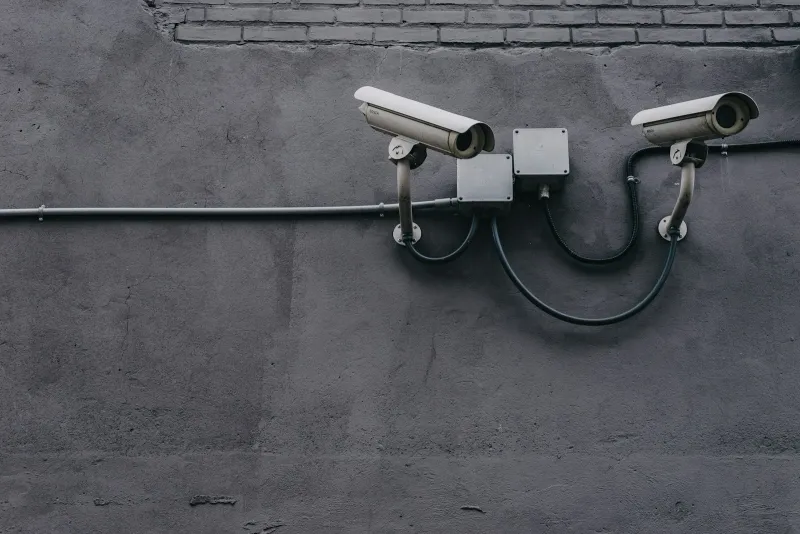 Two white security cameras mounted on a grey wall, linked by black cables and junction boxes