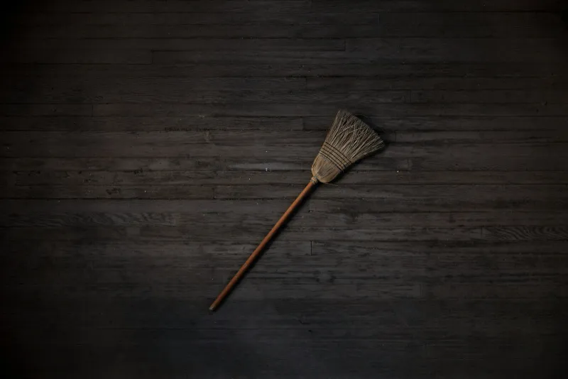 A traditional broom with a wooden handle lying on dark floorboards