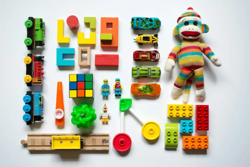 Colourful toy trains, blocks, cars and a knitted monkey arranged on a white background