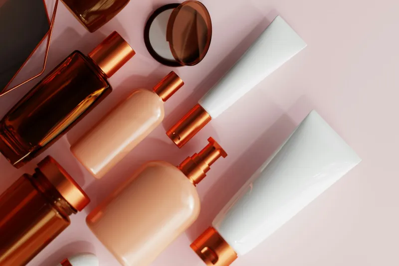 Unlabelled amber and peach skincare bottles and tubes on a pink background