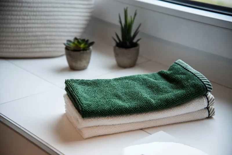 Folded green and white towels on a bathroom windowsill beside small potted plants