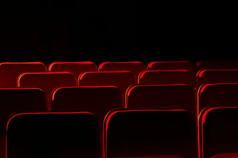 Rows of empty red theatre seats lit from the side in a dark auditorium