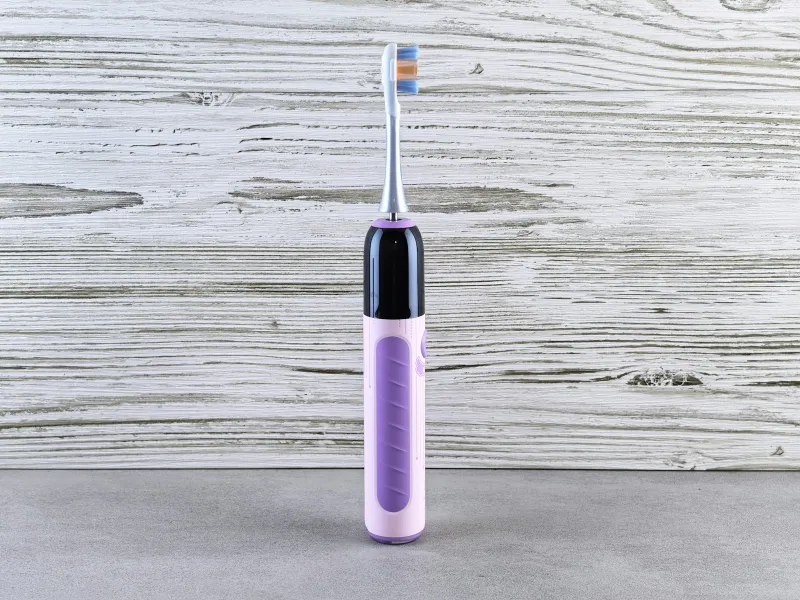 A purple electric toothbrush standing upright against a pale wooden background