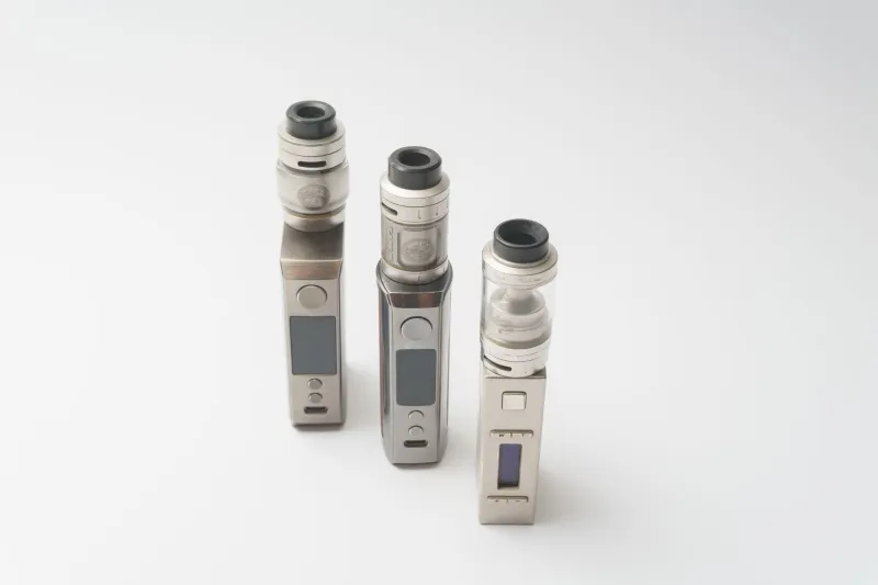 Three metal box-mod vape kits with tanks standing on a white background