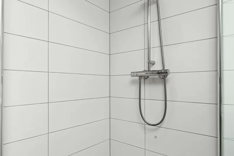 A white tiled walk-in shower with a chrome shower rail