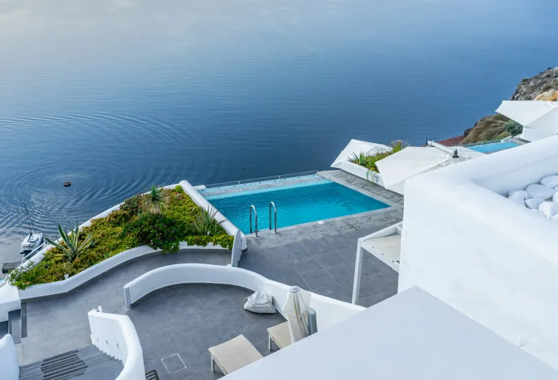 White-walled infinity pool overlooking the sea on a sunny day in Oia, Greece