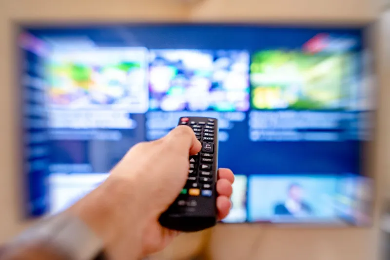 Hand pointing a remote control at a TV showing a streaming menu