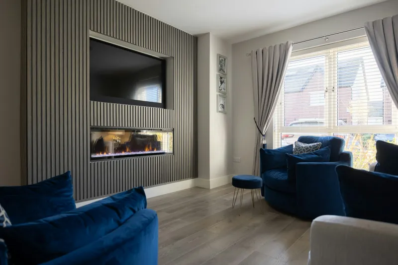 Living room with a grey slatted panel wall around a TV and fire, and blue velvet armchairs