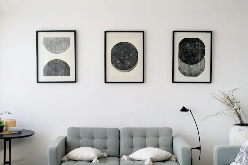 Three framed abstract prints hanging above a grey sofa in a bright living room