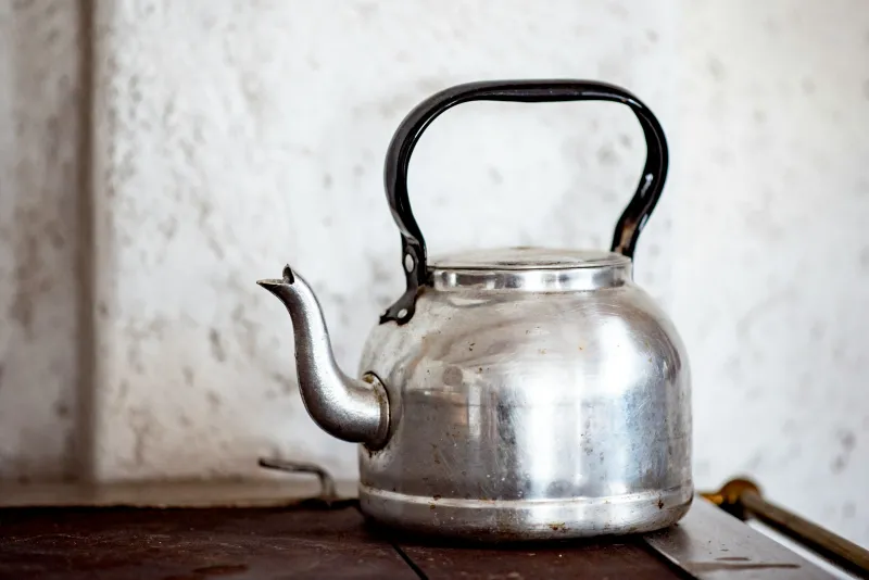 Stainless steel kettle with a black handle on a wooden surface