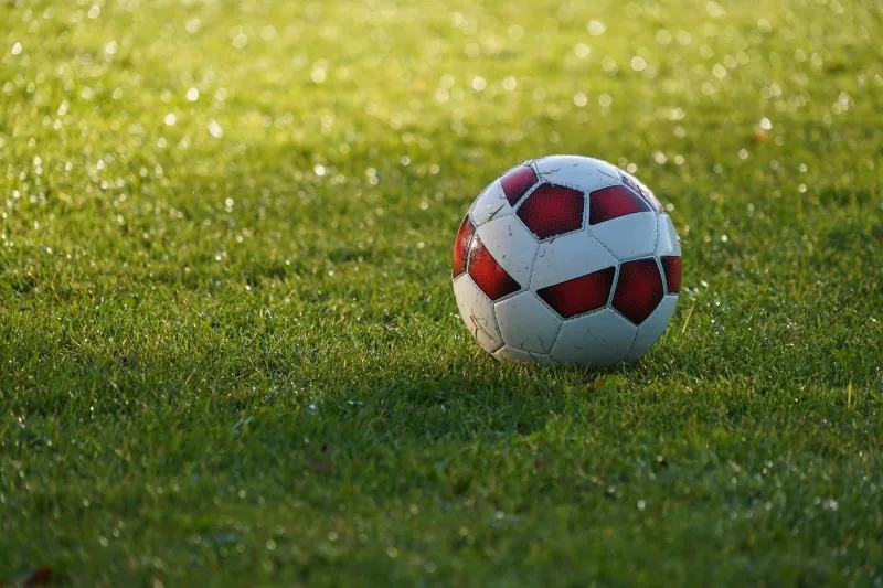 Red and white football on a sunlit grass pitch