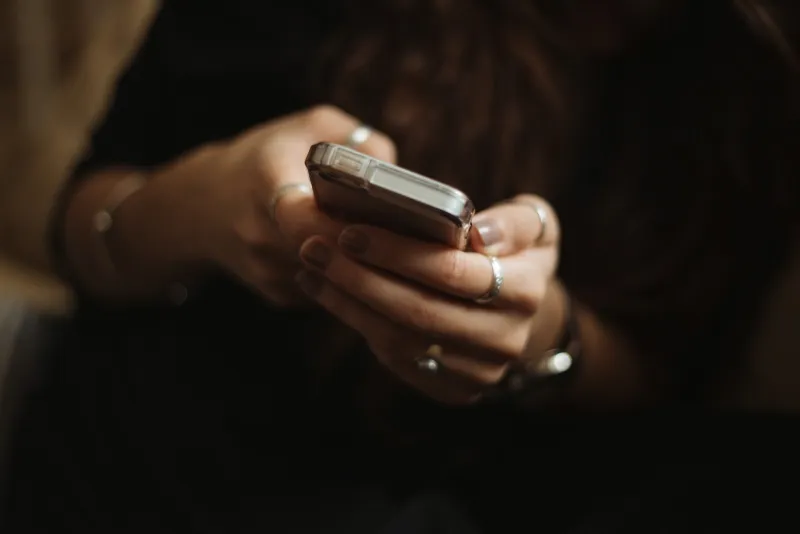 Close-up of hands with silver rings holding a smartphone in a dim room