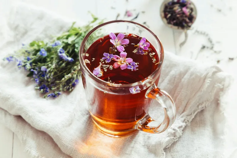 A glass mug of herbal tea with floating flowers beside a bunch of wild blooms