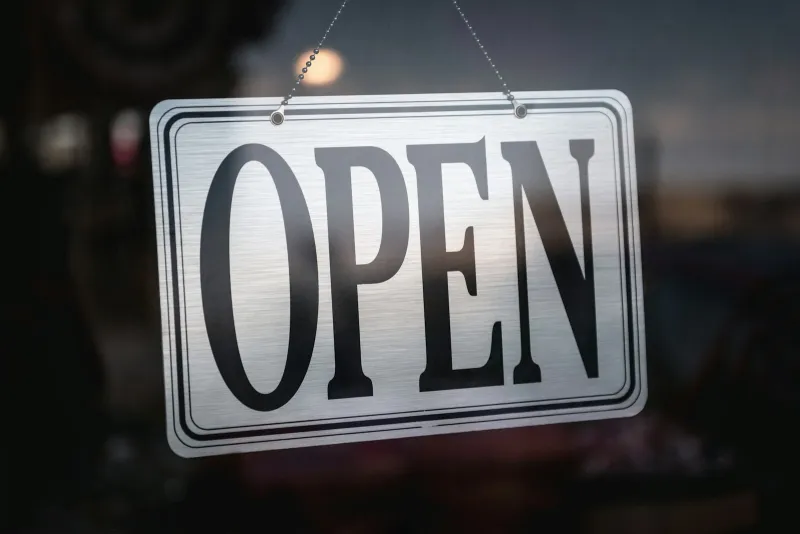 A metal Open sign hanging in a shop door