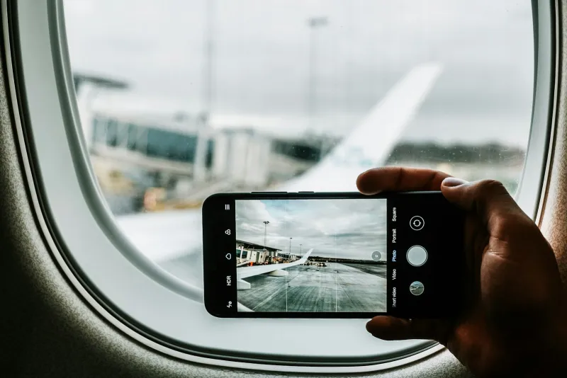 Hand holding a smartphone to photograph an aircraft wing through a plane window