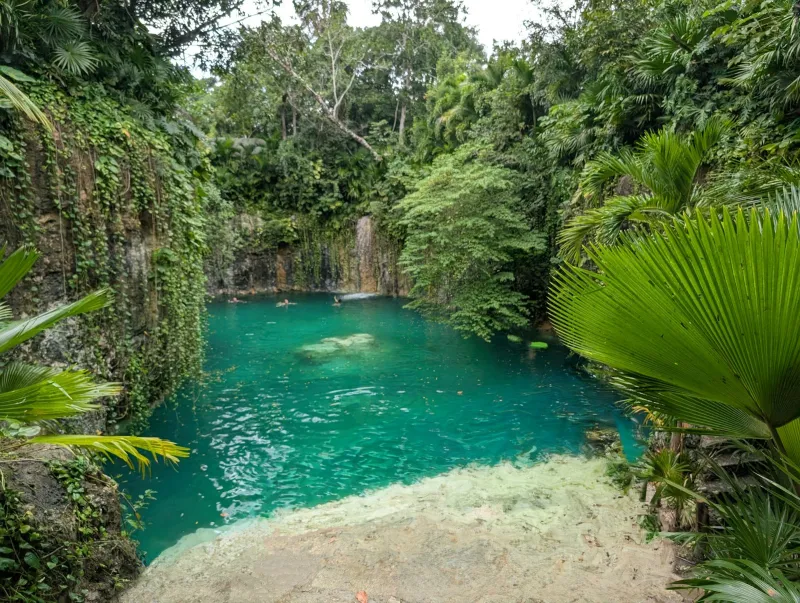 Xcaret: booking Riviera Maya parks and tours from the UK A turquoise cenote pool with a small waterfall, surrounded by jungle in Quintana Roo, Mexico