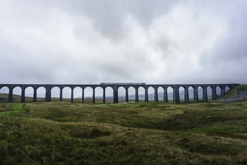 A train crossing a stone viaduct in the Yorkshire Dales on a cloudy day